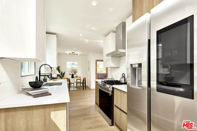 kitchen featuring stainless steel appliances, tasteful backsplash, wall chimney exhaust hood, light hardwood / wood-style flooring, and sink