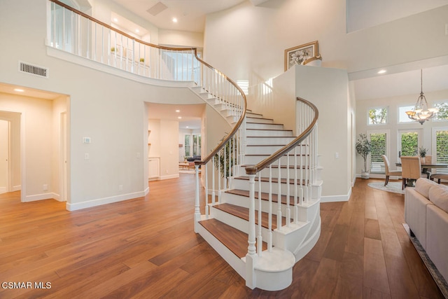 stairs with wood-type flooring, a towering ceiling, and an inviting chandelier