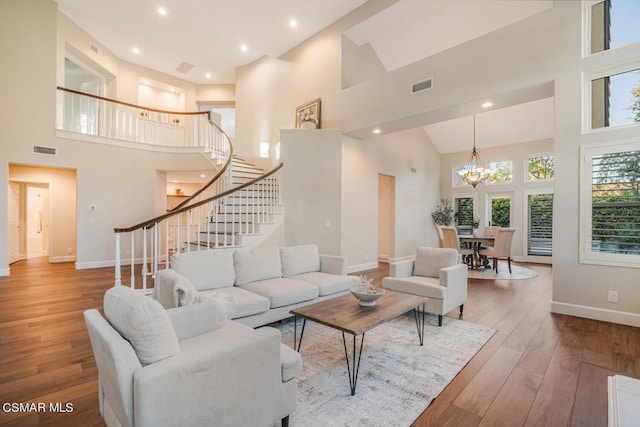 living room featuring a towering ceiling, an inviting chandelier, and hardwood / wood-style flooring