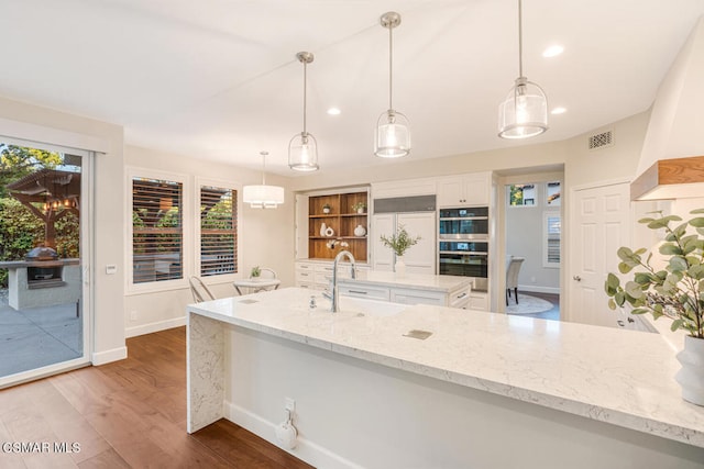 kitchen featuring white cabinetry, sink, light stone counters, and decorative light fixtures