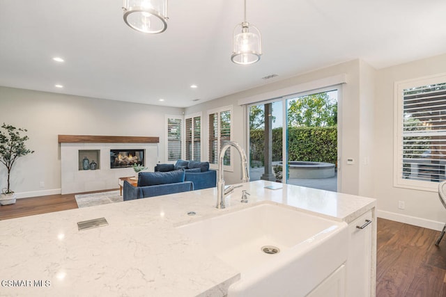 kitchen with pendant lighting, white cabinets, sink, dark hardwood / wood-style floors, and light stone counters