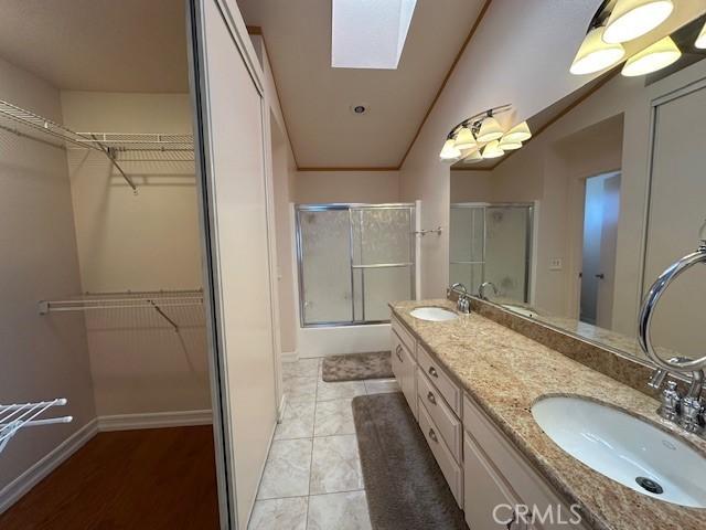 bathroom with a shower with shower door, vanity, vaulted ceiling with skylight, and tile patterned floors