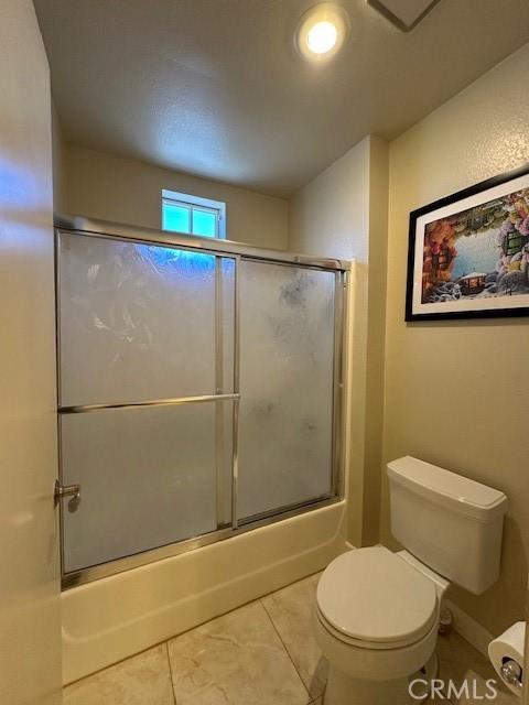 bathroom with toilet, tile patterned floors, and shower / bath combination with glass door