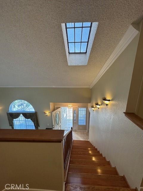 stairway featuring hardwood / wood-style flooring, a skylight, ornamental molding, and a textured ceiling