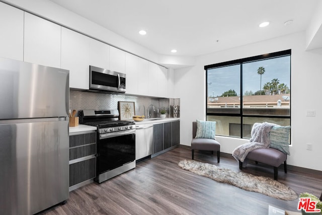 kitchen featuring appliances with stainless steel finishes, dark wood-type flooring, white cabinetry, sink, and backsplash