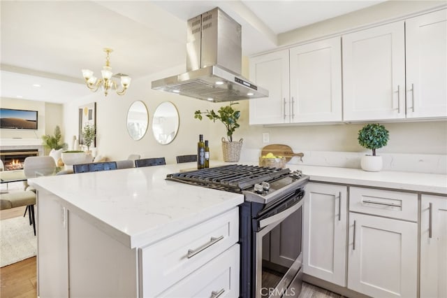 kitchen with a notable chandelier, stainless steel gas stove, white cabinets, and wall chimney range hood