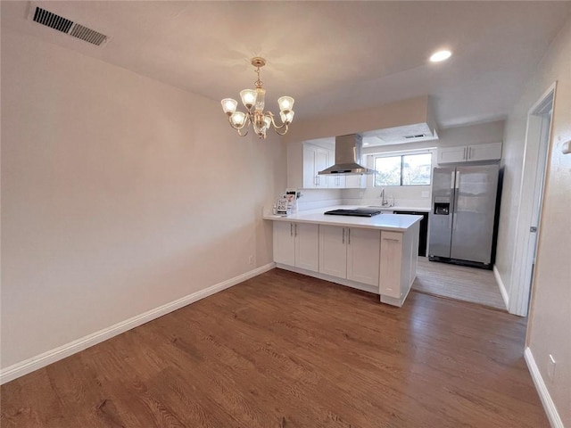 kitchen featuring white cabinets, wall chimney exhaust hood, hanging light fixtures, stainless steel fridge with ice dispenser, and kitchen peninsula