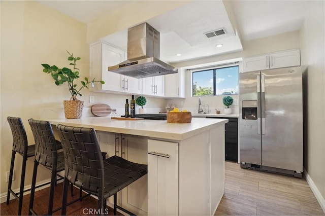 kitchen with stainless steel refrigerator with ice dispenser, a breakfast bar area, island range hood, and white cabinets