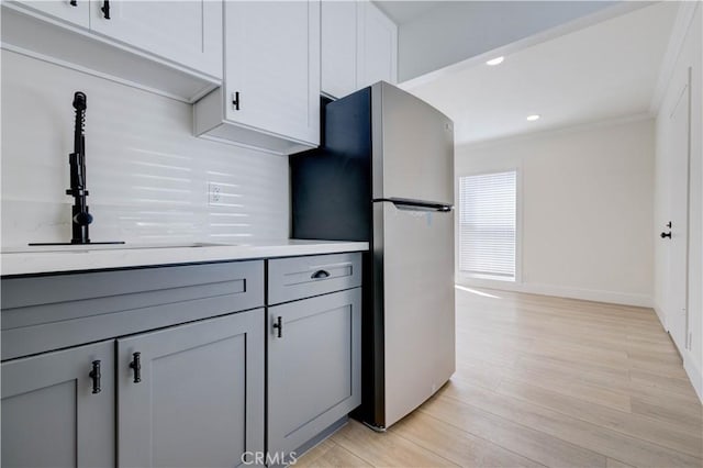 kitchen with sink, crown molding, white cabinetry, light hardwood / wood-style flooring, and stainless steel fridge