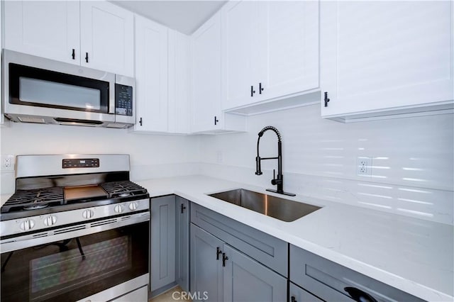 kitchen featuring white cabinetry, stainless steel appliances, gray cabinetry, light stone countertops, and sink