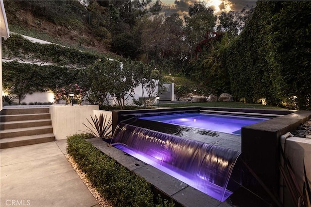 pool at dusk featuring pool water feature