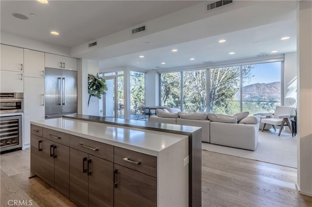 kitchen featuring a mountain view, appliances with stainless steel finishes, a wall of windows, wine cooler, and white cabinets