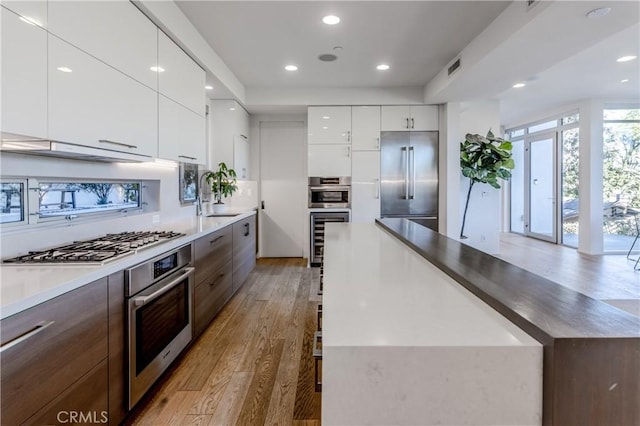 kitchen with white cabinetry, stainless steel appliances, light wood-type flooring, beverage cooler, and sink