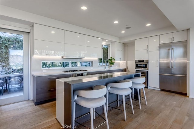 kitchen featuring dark brown cabinetry, white cabinets, a kitchen island, stainless steel appliances, and a breakfast bar area