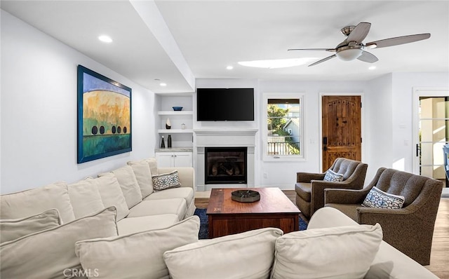 living room with ceiling fan, built in shelves, and hardwood / wood-style floors