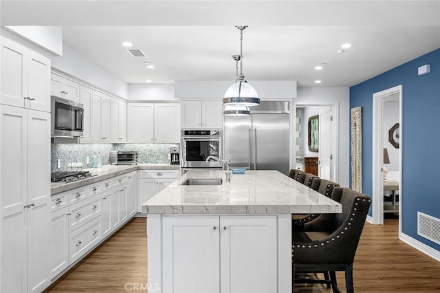 kitchen featuring a kitchen bar, white cabinets, appliances with stainless steel finishes, and an island with sink