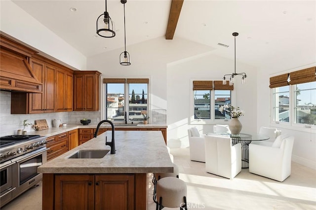 kitchen featuring decorative light fixtures, tasteful backsplash, a center island with sink, sink, and range with two ovens