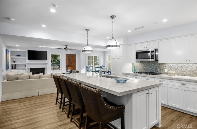 kitchen with a center island with sink, white cabinetry, hanging light fixtures, stainless steel appliances, and light stone counters