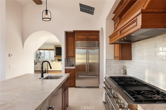 kitchen with custom exhaust hood, decorative backsplash, sink, high quality appliances, and light stone counters