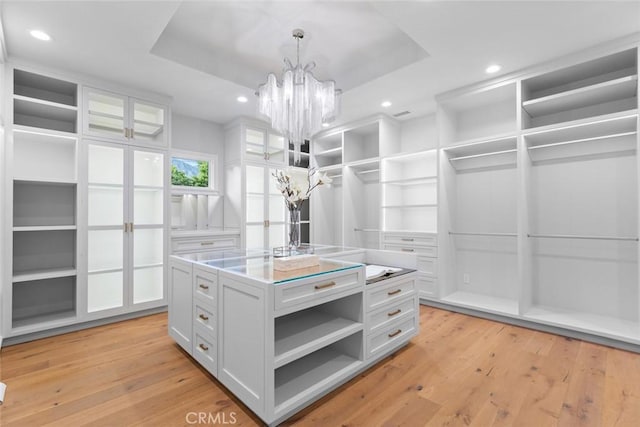 spacious closet featuring a tray ceiling, light hardwood / wood-style flooring, and a chandelier