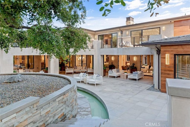 back of property with a balcony, a patio area, and an outdoor living space