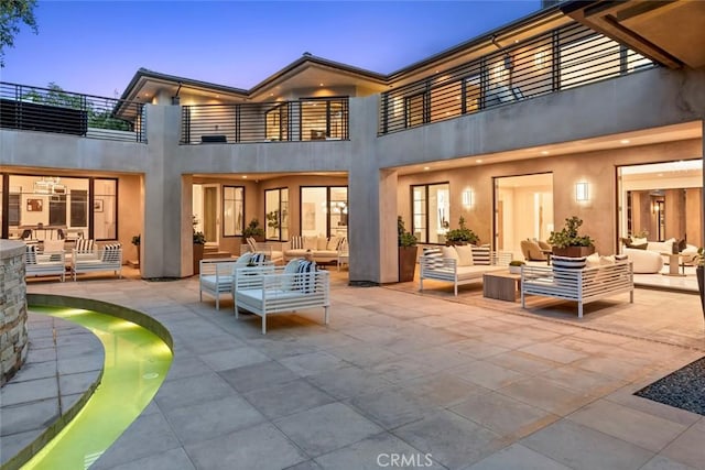 back house at dusk with a patio area, a balcony, and an outdoor hangout area