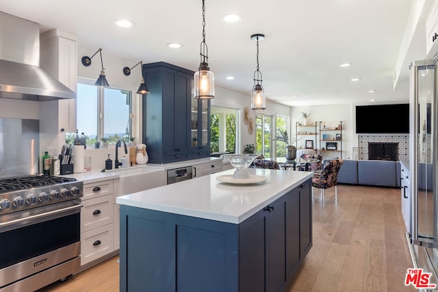 kitchen featuring white cabinetry, stainless steel appliances, a tiled fireplace, wall chimney exhaust hood, and sink