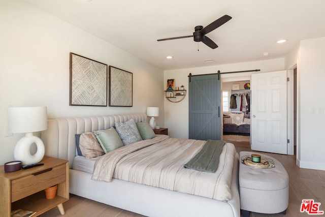 bedroom featuring a barn door, ceiling fan, a closet, wood-type flooring, and a walk in closet