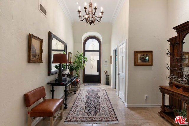 entryway with a towering ceiling, a notable chandelier, light tile patterned flooring, and ornamental molding