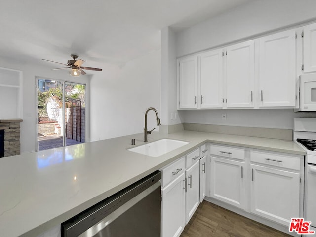 kitchen with ceiling fan, sink, white appliances, a stone fireplace, and white cabinets