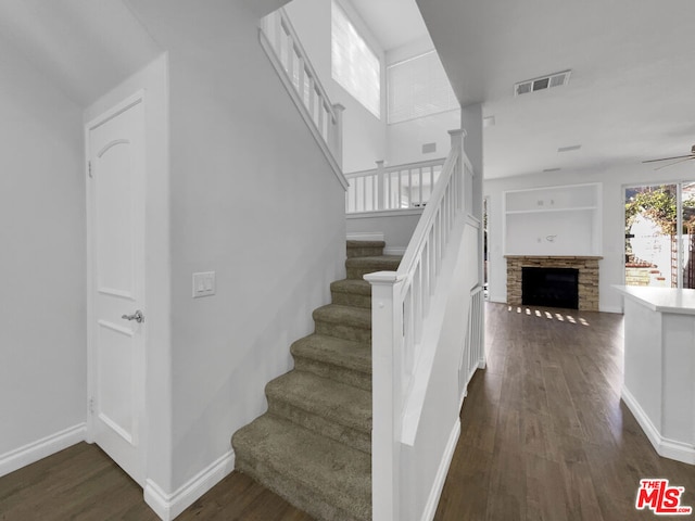 stairway featuring ceiling fan, built in shelves, a stone fireplace, and hardwood / wood-style flooring