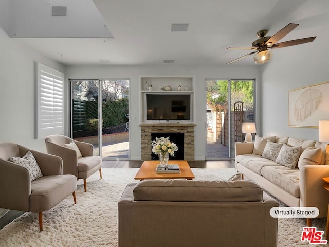 living room featuring ceiling fan, hardwood / wood-style flooring, built in features, and a stone fireplace