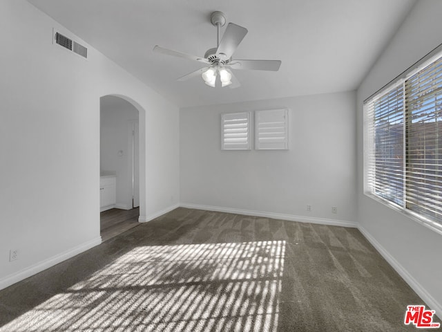 empty room with ceiling fan and dark colored carpet