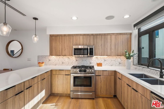 kitchen with stainless steel appliances, sink, backsplash, hanging light fixtures, and light hardwood / wood-style flooring