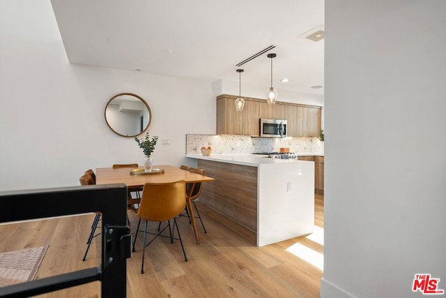 kitchen featuring decorative backsplash, light hardwood / wood-style floors, kitchen peninsula, and decorative light fixtures