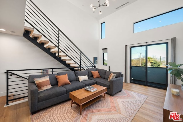 living room featuring a high ceiling, light wood-type flooring, and an inviting chandelier