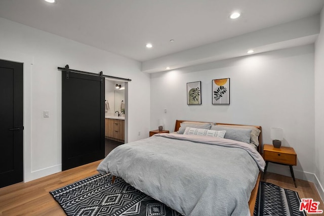 bedroom featuring connected bathroom, hardwood / wood-style floors, and a barn door