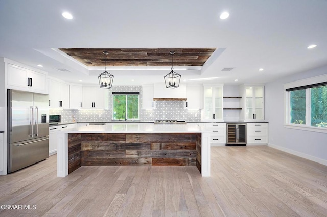 kitchen featuring built in fridge, a raised ceiling, white cabinets, and beverage cooler