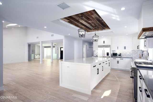 kitchen featuring a raised ceiling, white cabinetry, a kitchen island, and appliances with stainless steel finishes