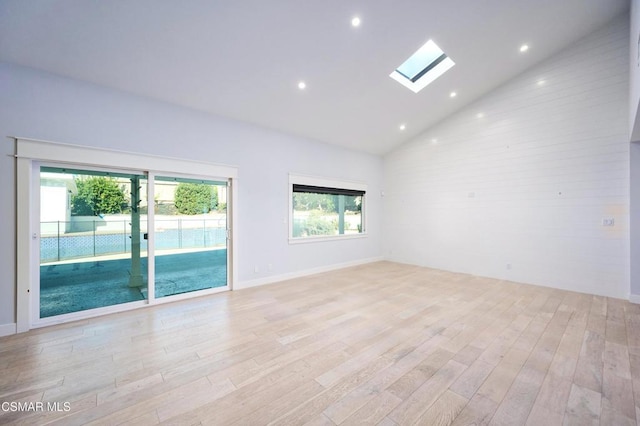 empty room featuring light hardwood / wood-style flooring, high vaulted ceiling, and a skylight