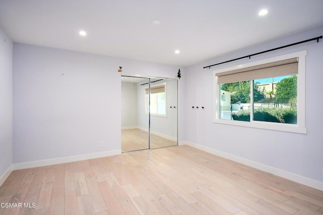 unfurnished bedroom featuring light hardwood / wood-style floors, multiple windows, and a closet