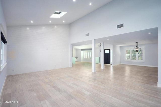 unfurnished living room with light hardwood / wood-style flooring, high vaulted ceiling, and a skylight