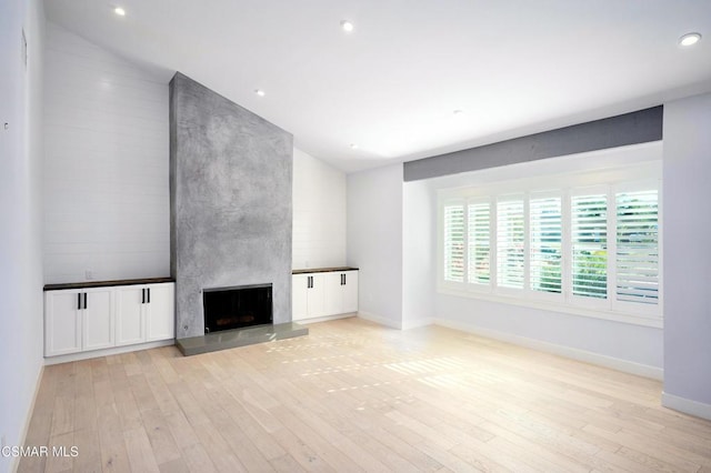 unfurnished living room with a large fireplace, lofted ceiling, and light hardwood / wood-style flooring