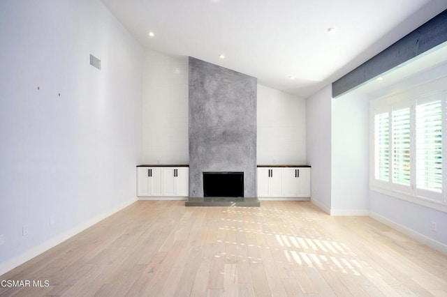 unfurnished living room featuring a fireplace, lofted ceiling, and light wood-type flooring