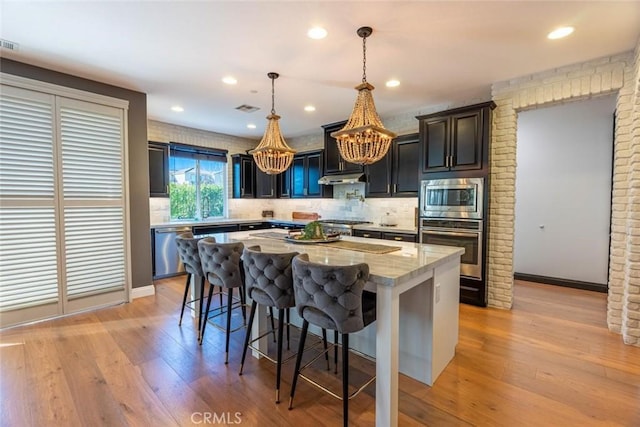 kitchen featuring pendant lighting, a center island, a kitchen bar, appliances with stainless steel finishes, and light stone counters