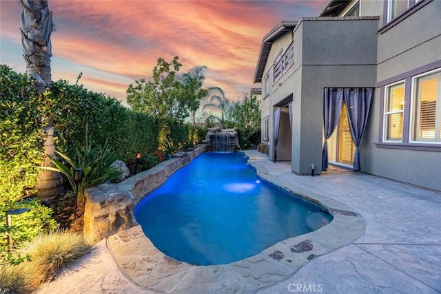 pool at dusk featuring pool water feature and a patio area