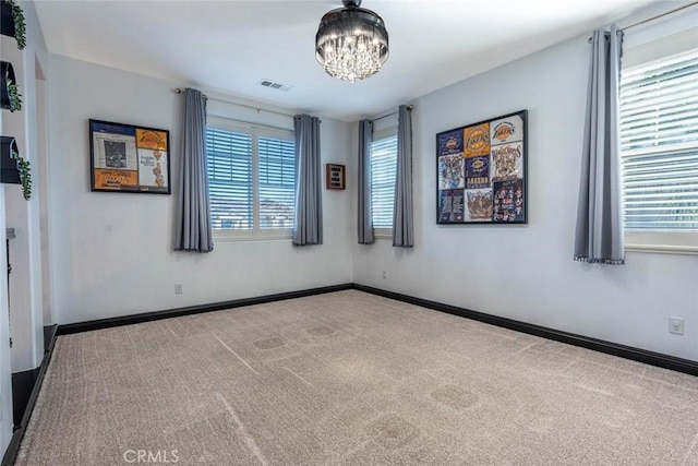 carpeted empty room with a wealth of natural light and a chandelier