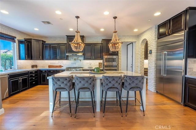 kitchen with decorative light fixtures, built in appliances, a breakfast bar area, and a kitchen island