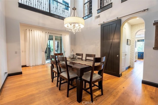 dining area with light wood-type flooring, a barn door, a towering ceiling, and a notable chandelier