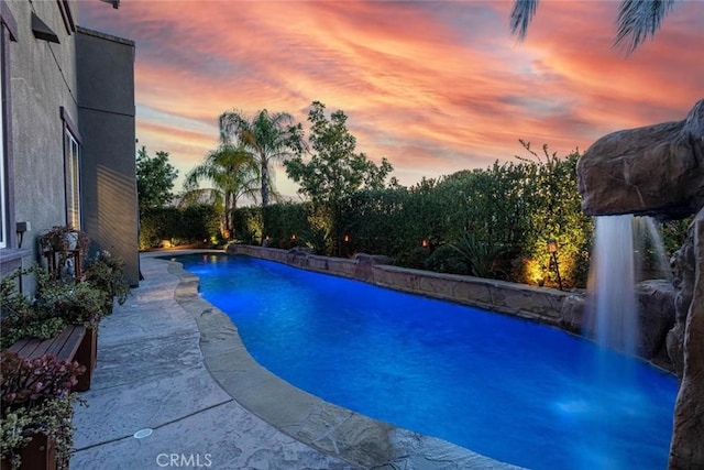 pool at dusk featuring pool water feature and a patio